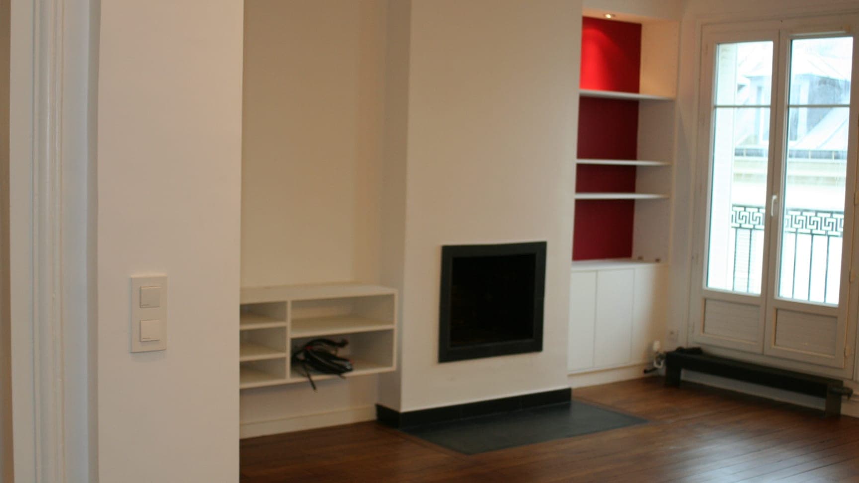 Séjour d'un appartement rénové : cheminée au foyer noir encastré, niches rouges et parquet foncé