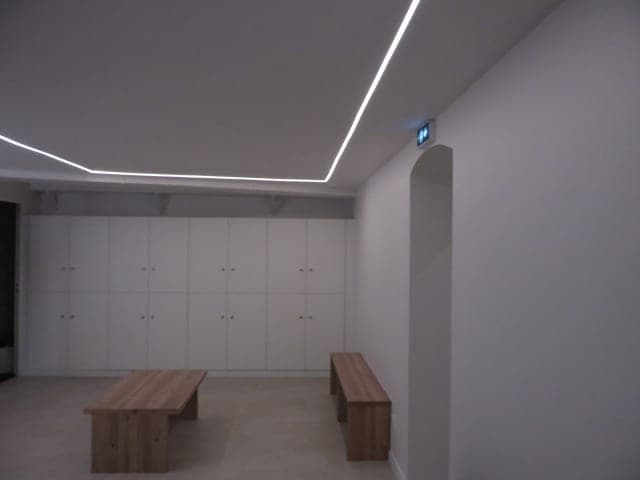 Vestiaire aux casiers blancs toute hauteur, deux bancs en bois massif et ligne lumineuse en périphérie du plafond