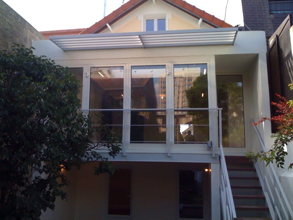 Façade arrière d'une maison : pièce vitrée à brise-soleil à lames, escalier extérieur blanc et jardin
